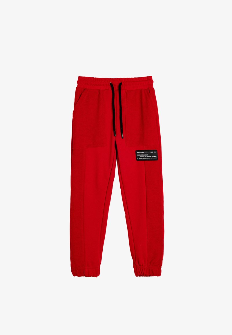 Red sweatpants made of soft fabric, featuring an elastic waistband, drawstring closure, and two side pockets. Black accent patch displayed on leg.