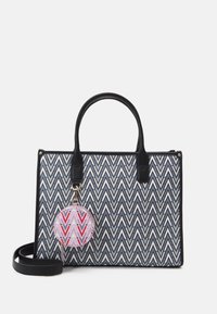 Sac fourre-tout à motif zigzag noir et blanc avec des poignées noires et un porte-clés rond détachable, arborant un design géométrique rose et rouge.