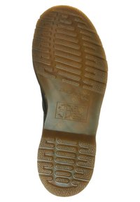 Suela de zapato de goma negra con una superficie texturizada, que presenta franjas horizontales y verticales elevadas, y un emblema de logo en el centro.