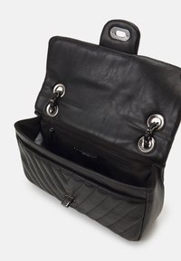 Borse a mano in pelle nera con design trapuntato, hardware in tonalità argento, chiusura magnetica e tasca interna con zip. Aperta per visibilità.