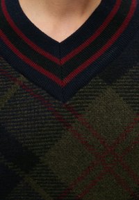 Pull à col en V avec un col rayé bleu marine, noir et bordeaux et un motif losanges vert foncé et rouge sur le tissu.