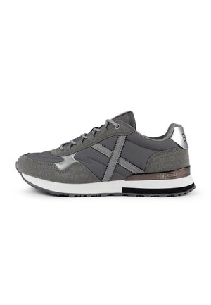 Chaussure de sport grise présentant un mélange de matériaux lisses et texturés, avec des accents métalliques et une semelle blanche rembourrée.