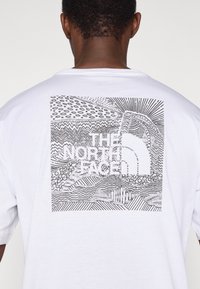 Λευκό βαμβακερό t-shirt με μαύρο γραφικό σχέδιο. Το σχέδιο περιλαμβάνει αφηρημένα μοτίβα και το λογότυπο "THE NORTH FACE" στο κέντρο.