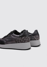 Zapatillas negras y grises con parte superior metálica, talón con estampado de leopardo texturizado y suela de goma gris. Presenta cordones negros y acentos trenzados.