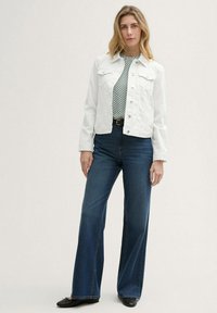 Veste en denim blanche sur un top à motifs noir et blanc, associée à un jean flare bleu foncé taille haute et des ballerines noires.