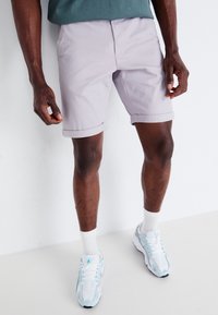 Shorts lavande clair avec des revers, fabriqués à partir d'un tissu doux ; associés à des chaussettes blanches et des chaussures de sport multicolores.