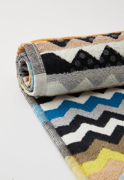 Fargerik håndkle med zigzag-mønster laget av myk frotté. Har sterke farger av blå, svart, gul og beige med en teksturert finish.