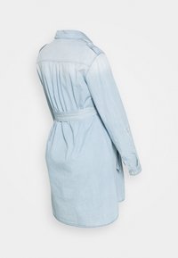 Ljusblå denimklänning med en lätt urtvättning, bälte i midjan, långa ärmar och krage vid halsen. Den har en rundad nederkant.