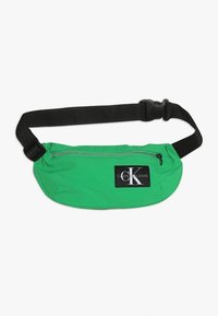 Zielona nerka wykonana z lekkiego materiału. Posiada czarny regulowany pasek i srebrny zamek błyskawiczny. Wyposażona w naszywkę z logo Calvin Klein Jeans.