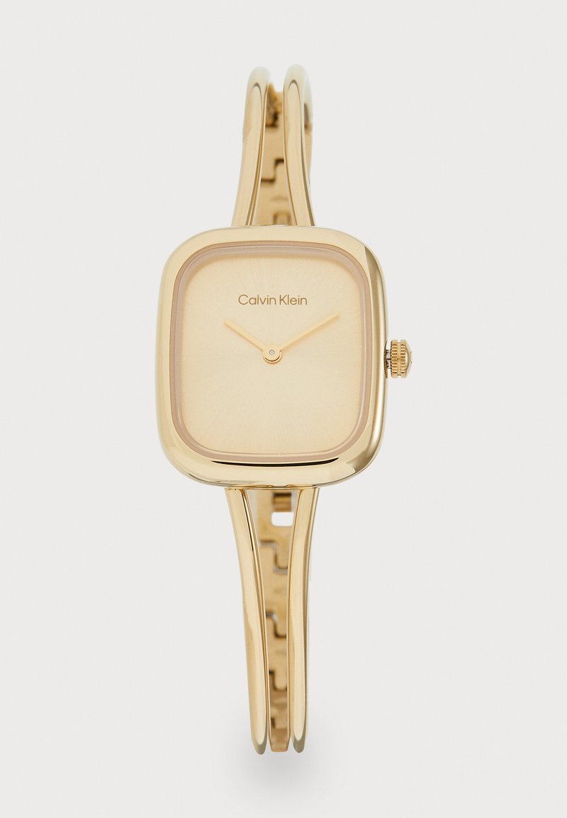 Gold-tone square watch with a smooth dial, slender metal band, and a subtle branding detail. Features a simple crown for adjustment.