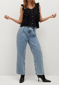 Top senza maniche nero con spalline arricciate e chiusura a bottoni, abbinato a jeans a gamba larga azzurri a vita alta e stivaletti neri con punta affusolata.