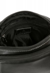 Interno di una borsa in pelle nera con una fodera in tessuto. Presenta una tasca con zip e un'etichetta. Dettagli cuciti lungo la zip. Texture liscia.