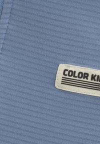 Ljusblå, ribbad tyg med en strukturerad yta; har en vit etikett med svart text som läser "COLOR KID" och ränder.