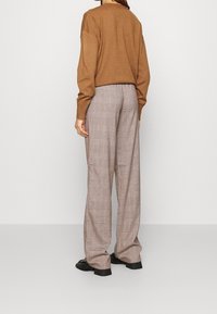 Brown knitted sweater with long sleeves paired with wide plaid trousers in brown, beige, and dark colors. Black footwear complements the outfit.