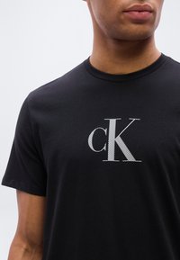 Μαύρο βαμβακερό T-shirt με μεγάλο, λευκό κεντητό λογότυπο 'cK' στο στήθος. Κοντά μανίκια και σχέδιο με στρογγυλή λαιμόκοψη.