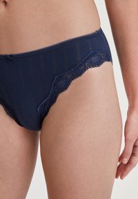 Marineblauwe katoenen slipjes met kantafwerking, met verticale strepen en een gebogen rand. Zachte textuur en decoratieve strikdetail op de tailleband.