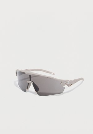 Jasnoszare sportowe okulary przeciwsłoneczne z owijkowymi ciemno przyciemnianymi soczewkami i elastycznymi zausznikami na białym tle.