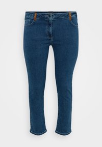 Blue denim jeans with a slim fit, featuring a zip fly, brown leather accents at the waist, and contrast stitching. Classic five-pocket design.