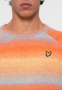 Maglione a coste con una sfumatura di arancione e azzurro chiaro, colletto rotondo e logo di un uccello ricamato giallo sul lato sinistro del petto.