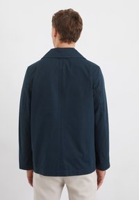 Marineblå bomuldsjakke med skåret krave, lange ærmer og en glat tekstur. Har en skræddersyet pasform og subtile syninger.
