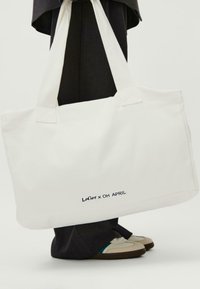 Baltas drobės rankinis krepšys su siuvinėjimo detalėmis ir užrašu "Lefter x OH APRIL". Tvirti rankenų ir plokščia konstrukcija.