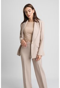 Beżowy garnitur o dopasowanym kroju z jednorzędową marynarką i prostymi spodniami. Miękka faktura, gładka tkanina i minimalistyczny design.