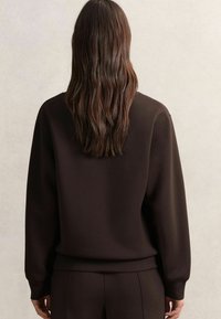 Sudadera marrón con un corte relajado, puños y dobladillo acanalados. Fabricada con un tejido suave, presenta un diseño simple con un mínimo de detalles.