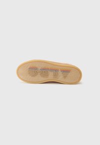 Shoe sole featuring a tan rubber material with a textured pattern. Pink upper rubber layer with multicolored stripe details and logo.