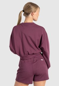 Completo due pezzi marrone scuro composto da una maglietta a maniche lunghe a vestibilità ampia e pantaloni corti con vita elastica, realizzato in un tessuto morbido con una superficie liscia.