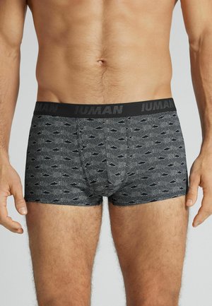 Mandlig overkrop iført grå boksershorts med sorte abstrakte bølgede og hajmønstre, mærket elastik i taljen på lysegrå baggrund.