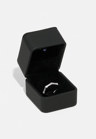 Black hexagonal ring box with a textured finish. Inside, a silver ring featuring a bar design with small sparkling accents on a dark velvet lining.