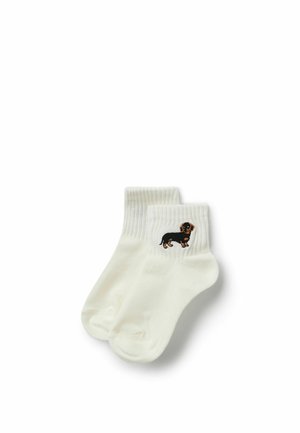 Weiße Knöchelsocken mit gerippten Bündchen und einem kleinen bestickten schwarzen und braunen Dackel auf dem Bündchenbereich.