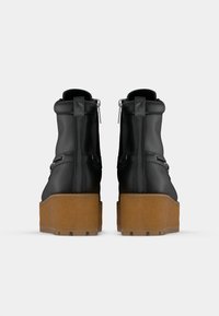 Czarne botki za kostkę o matowym wykończeniu, z grubą brązową platformą, bocznymi zamkami i smukłym designem z minimalną ilością ozdób.