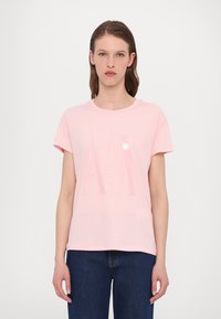 Gaiši rozā īsām piedurknēm T-krekls, izgatavots no mīksta auduma. Priekšpusē ir spīdīgs "AX" logos un "ARMANI EXCHANGE" teksts.