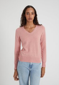 Pull en V rose en tissu doux avec des manches longues et un ourlet côtelé. Associé à un jean bleu clair pour un look décontracté.