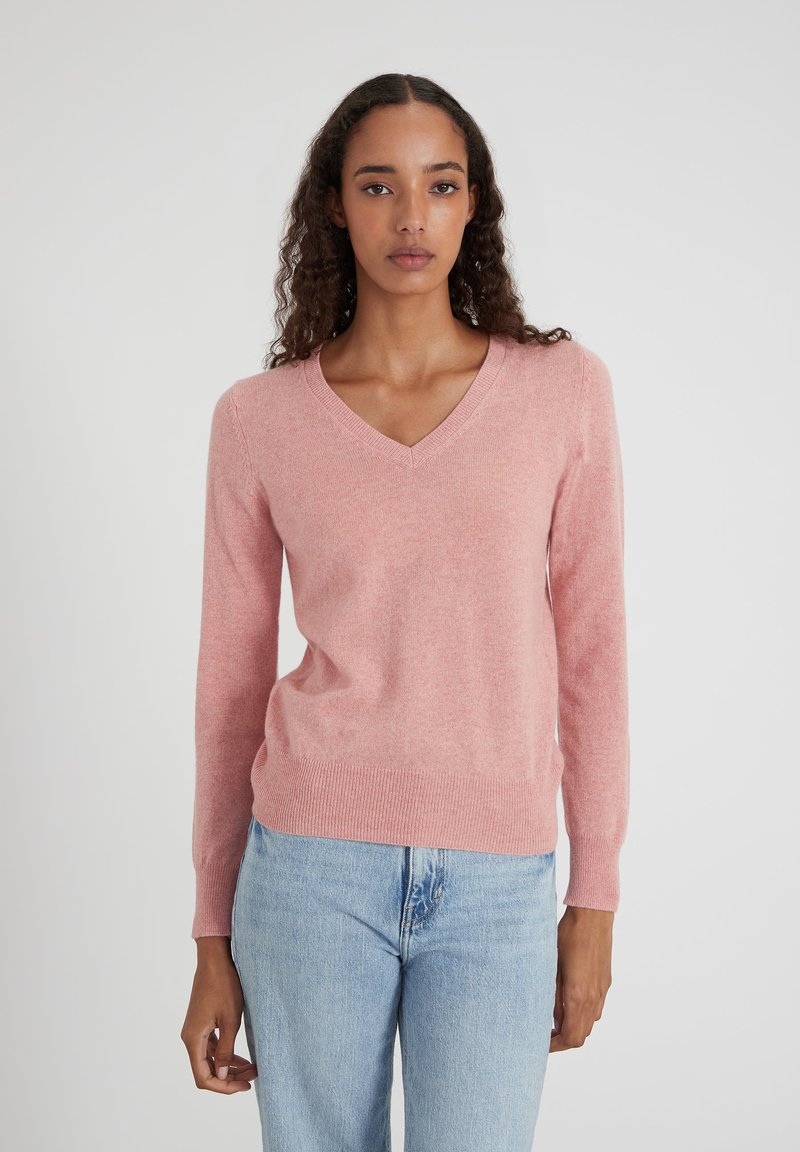 Pull en V rose en tissu doux avec des manches longues et un ourlet côtelé. Associé à un jean bleu clair pour un look décontracté.