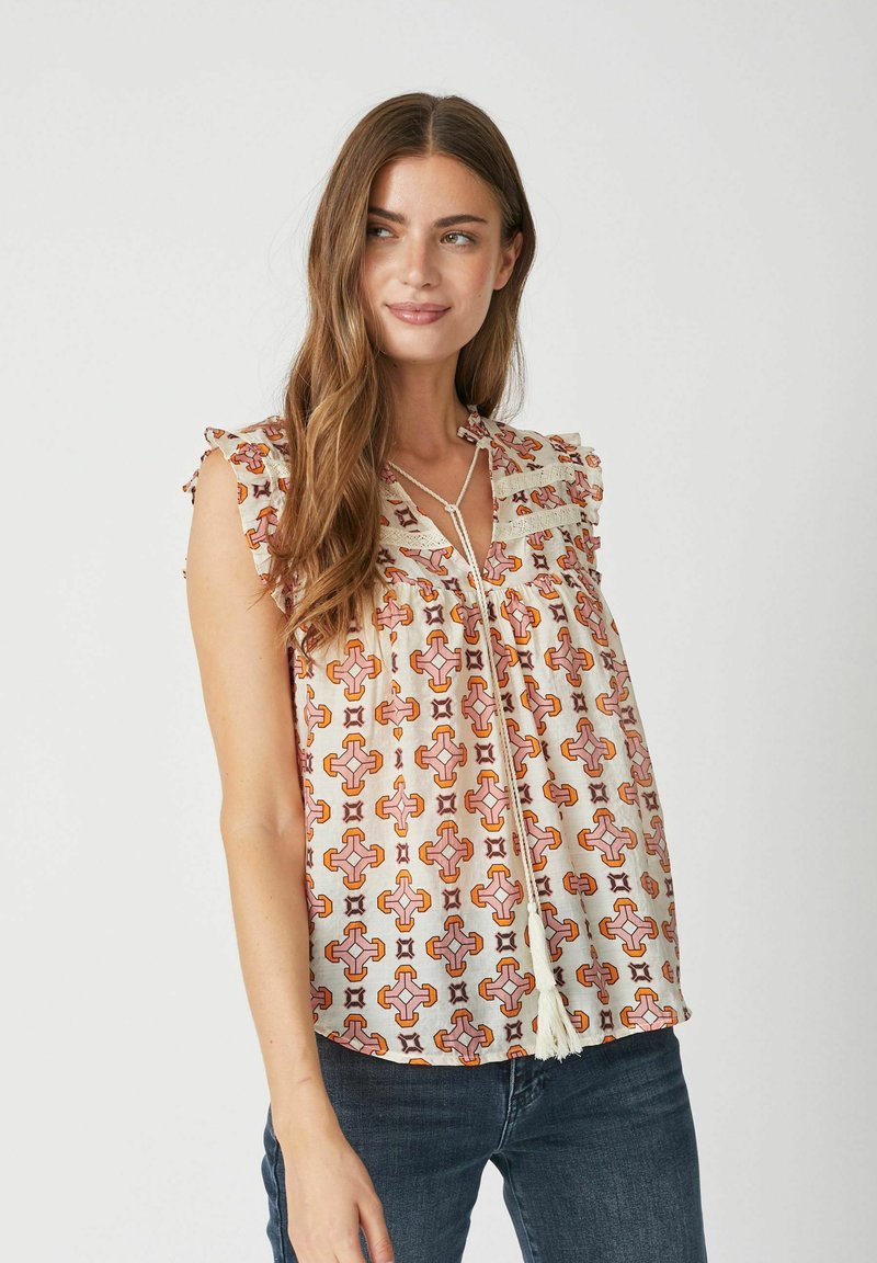Blusa leggera in crema con motivi geometrici arancioni e rosa, maniche arricciate e dettaglio con nodo frontale.