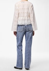 Chemisier blanc brodé avec des manches cloche longues, un ourlet festonné et des motifs en œillets détaillés, associé à un jean en denim bleu taille haute.