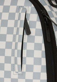 Zaino in tessuto a quadri blu e bianchi con una cerniera nera, dotato di una tasca a soffietto orizzontale e un tirazip con marchio.