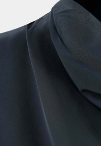 Gros plan d'un tissu foncé avec une texture douce et fluide et des plis délicats créant un drapé en couches.