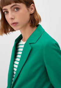 Green tailored blazer with a notched collar and smooth texture, overlaid on a white shirt with green horizontal stripes.