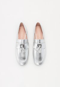 Hõbedased nahast loafersid siledal viimistlusel, millel on tõmbluku aktsent ja väike must metalldetail ees.