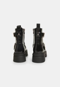 Botas cortas de charol negro con suela de goma gruesa, que cuentan con hebillas ajustables en los laterales y acentos texturizados en los costados.