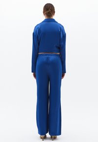 Blå satinkostym i två delar bestående av en cropped blus med krage och vida byxor med elastisk midja. Slät, glänsande textur.