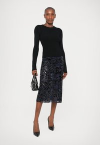 Top negru din tricot cu mâneci lungi, asortat cu o fustă bleumarin până la genunchi, acoperită cu paiete. Prezintă o siluetă ajustată. Accesoriile includ o geantă mică neagră.