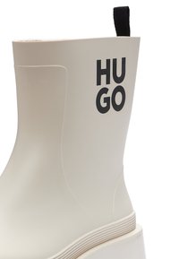 Witte rubberen regenschoen met een plat ontwerp, opvallend "HUGO" logo en een geprofileerde zool. Voorzien van een zwarte trekband aan de achterkant.