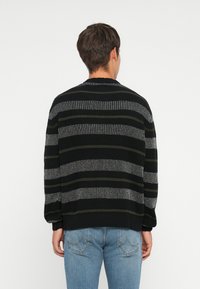 Black and gray striped sweater with a relaxed fit, ribbed texture, and round neckline, paired with light blue jeans.
