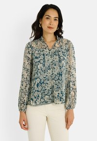 Blouse à motif floral en bleu sarcelle foncé et crème, avec un col, une fermeture à boutons sur le devant, des manches longues et un tissu léger et transparent.