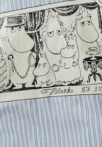 Kokvilnas audums ar melnbaltu Mūmiņu tēlu grafiku uz krēmkrāsas fona ar zilām svītrām, ieskaitot dekoratīvu galdu.