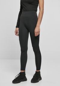 Leggings noirs avec une taille haute, fabriqués en matériau extensible, présentant une texture côtelée sur les panneaux latéraux et une coupe ajustée.
